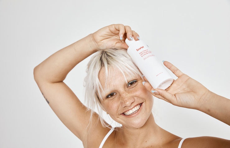 A woman with blonde hair holding a bottle of Scarlet's skincare